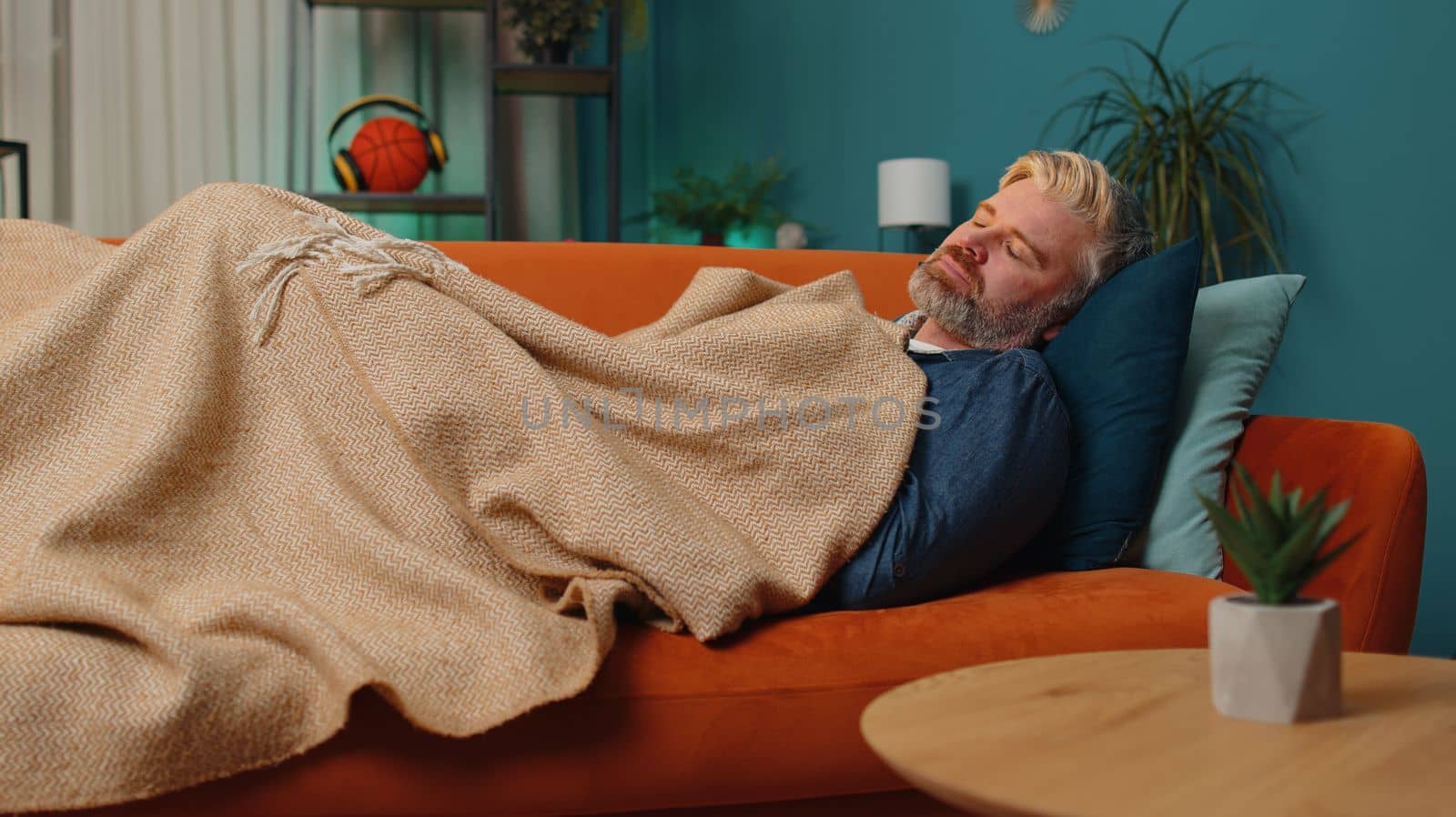 Tired middle-aged man lying down in bed taking a rest at home. Carefree mature senior gray-haired guy napping, falling asleep on comfortable sofa with pillows. Closed his eyes enjoy night nap alone