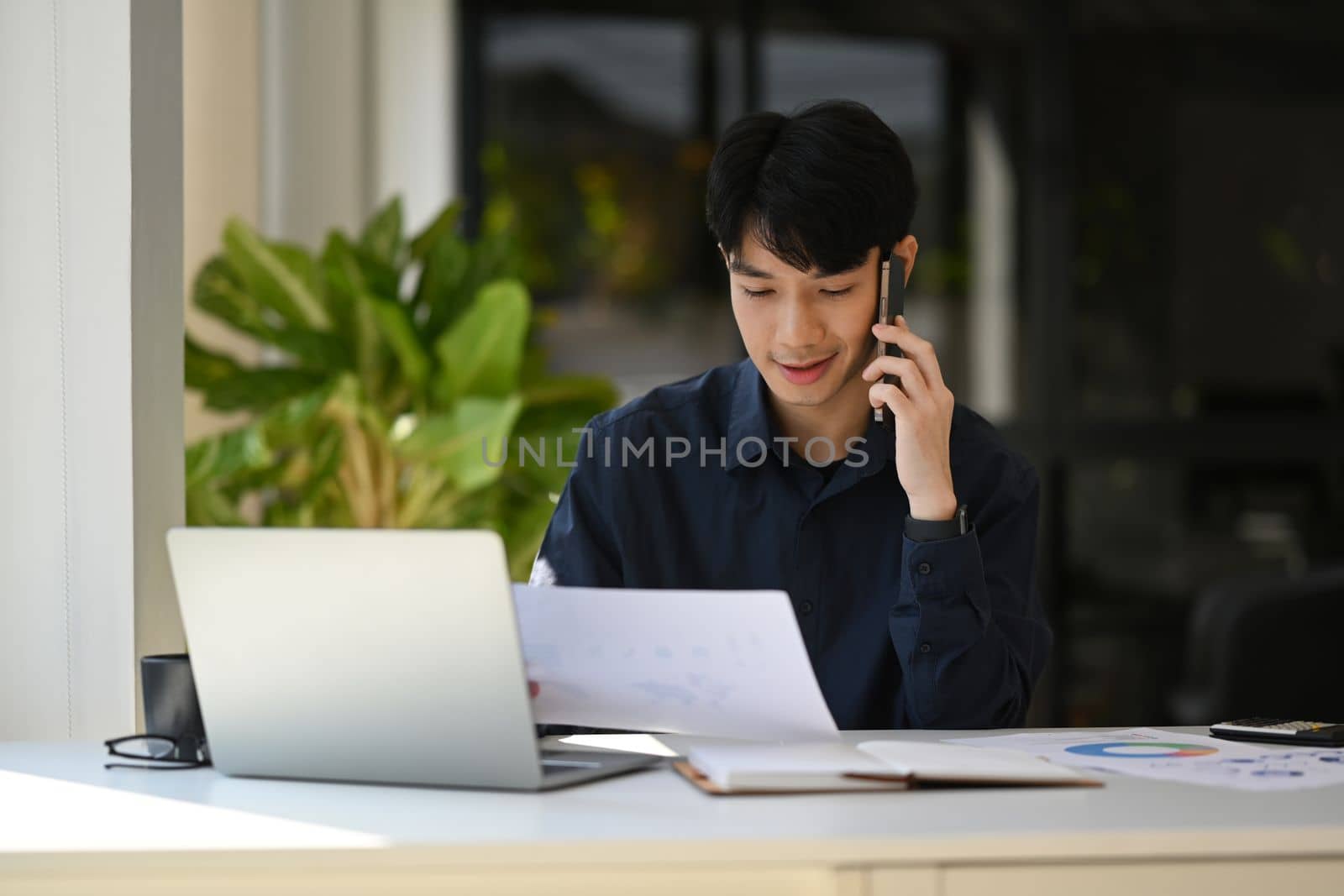 Handsome male financial advisor looking at document and talking on mobile phone with client.