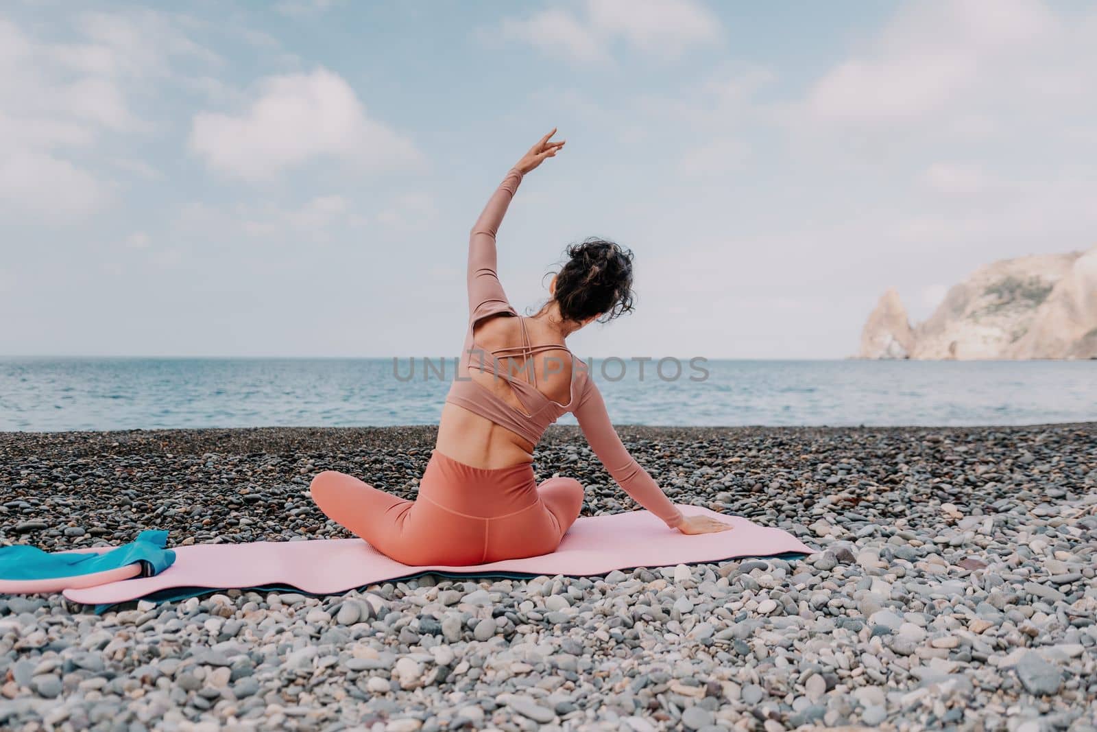 Middle aged well looking woman with black hair doing Pilates with the ring on the yoga mat near the sea on the pebble beach. Female fitness yoga concept. Healthy lifestyle, harmony and meditation.