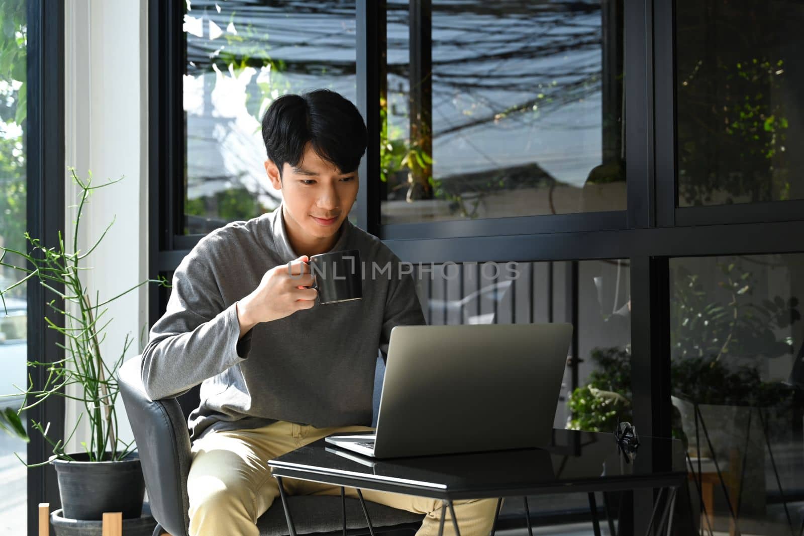 Pleasant man in warm clothes drinking coffee and checking email on laptop computer.