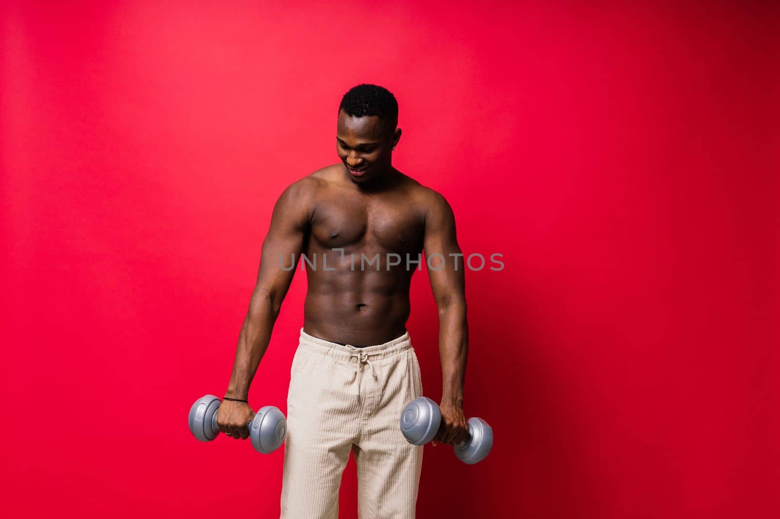 Portrait of a happy african man with dumbbells over red background by Zelenin
