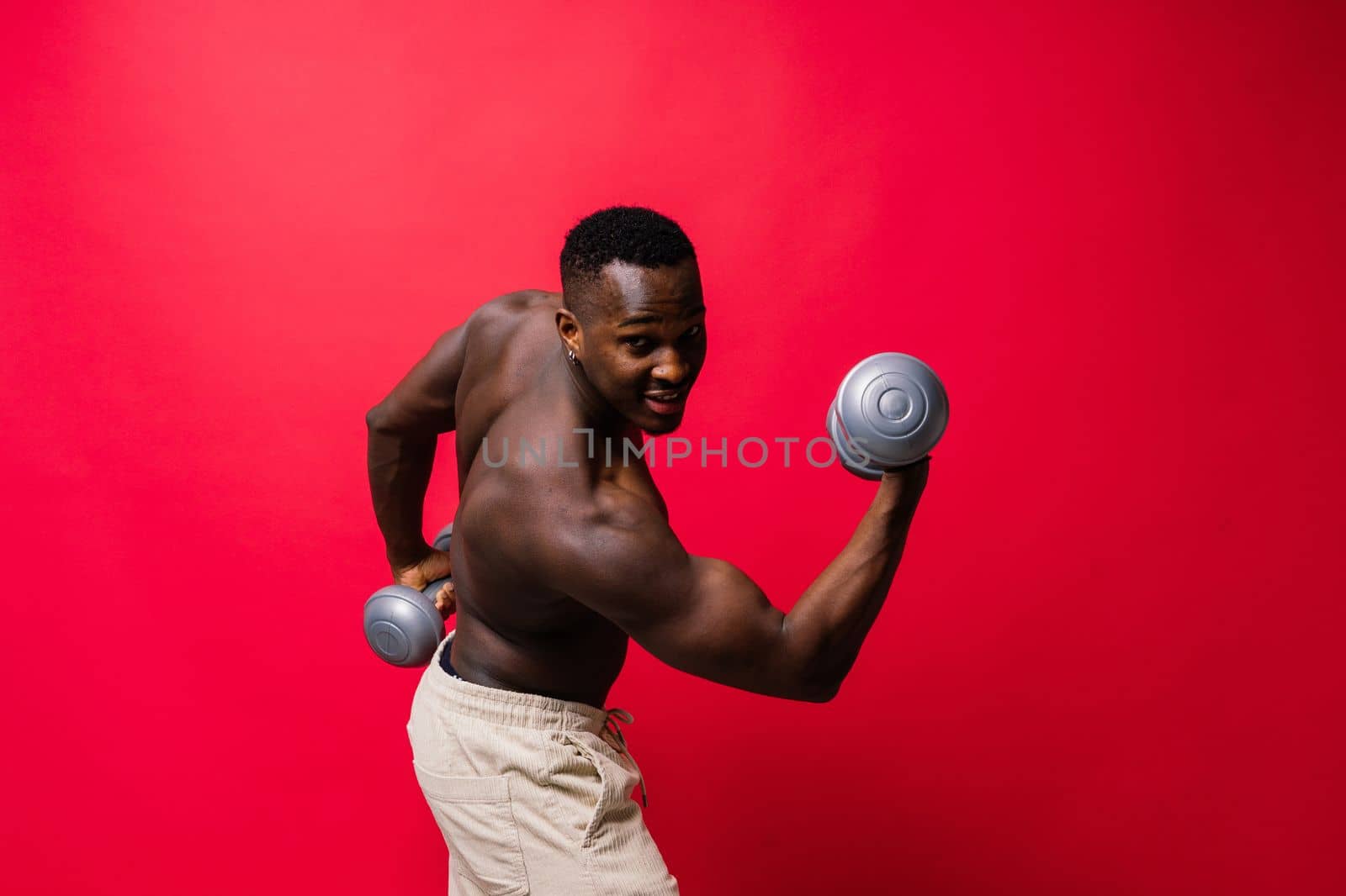 Portrait of a happy african man with dumbbells over red background by Zelenin