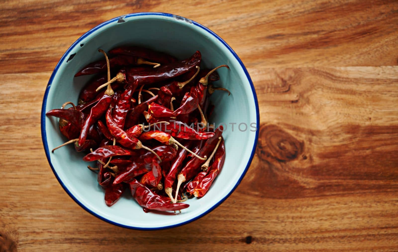 Intensely spicy. High angle shot of dried red chillies in a bowl on a kitchen counter. by YuriArcurs