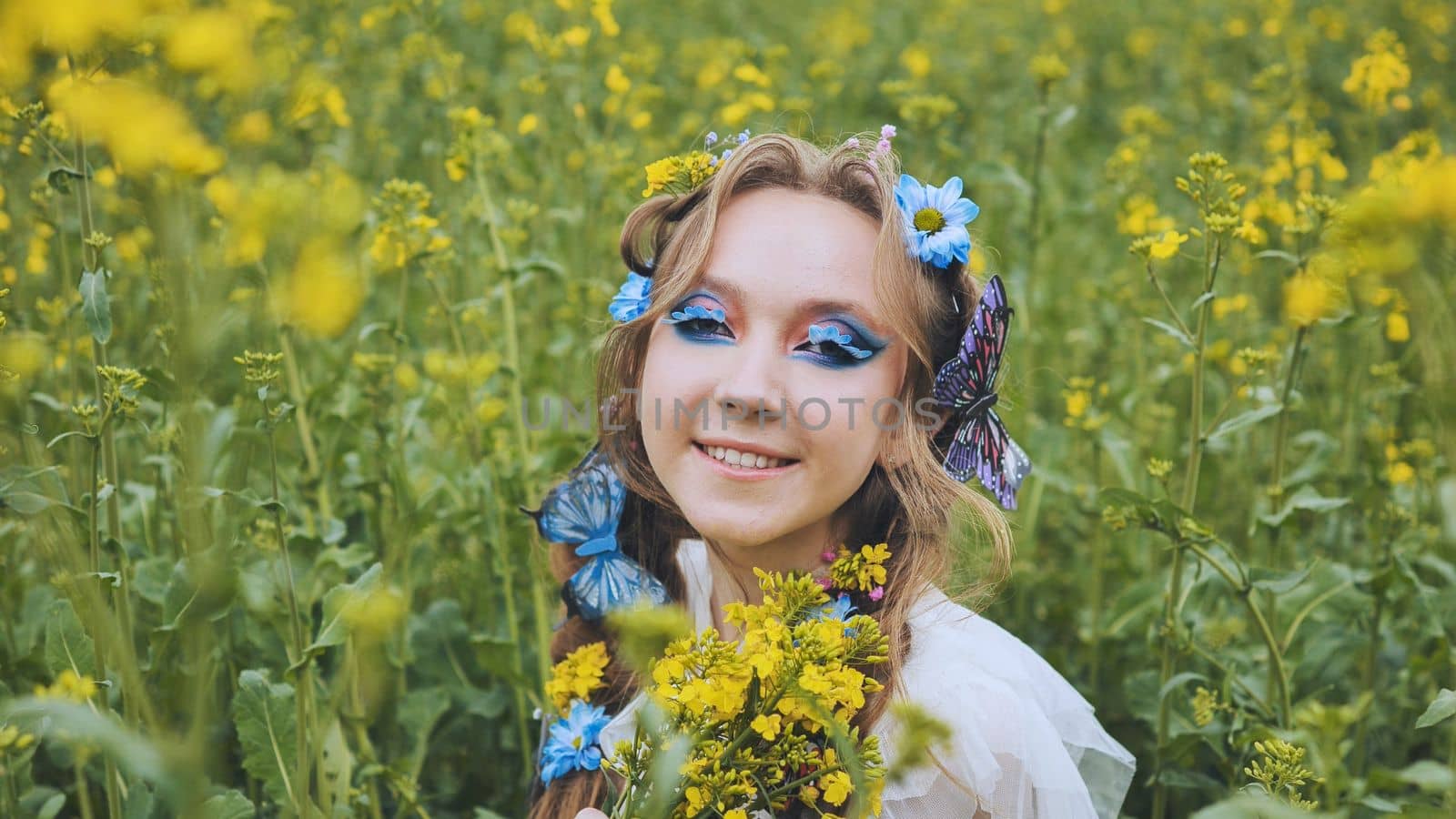 A young girl poses in a rapeseed field with a beautiful hairdo of flowers and butterflies