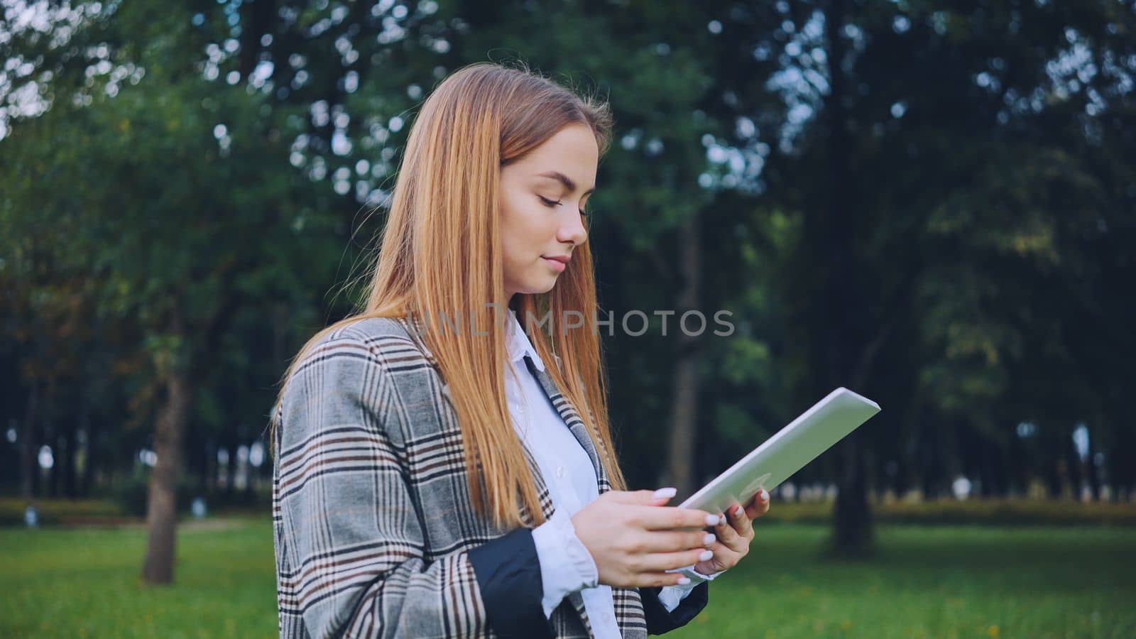 A young girl walks with a tablet in the park