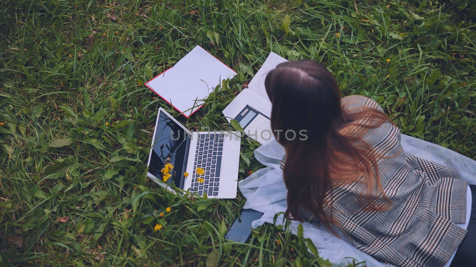 A young student with notebooks and a laptop lying on the grass
