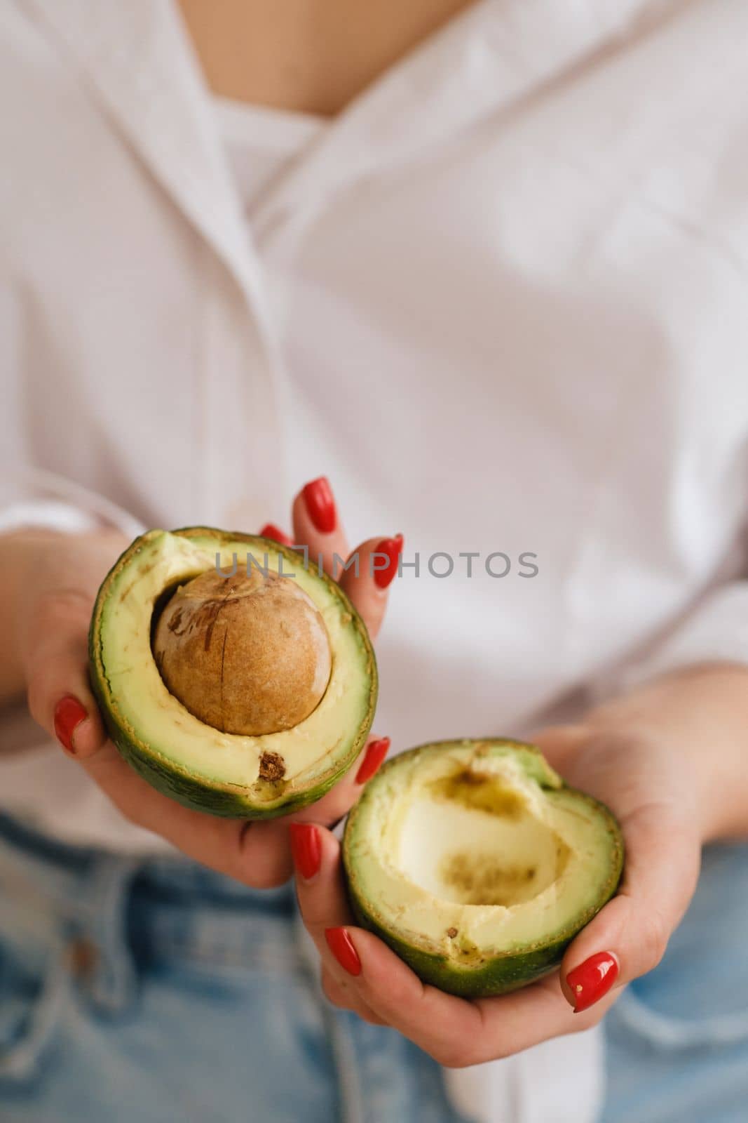 Close-up of a girl's hand holding an avocado cut in two.