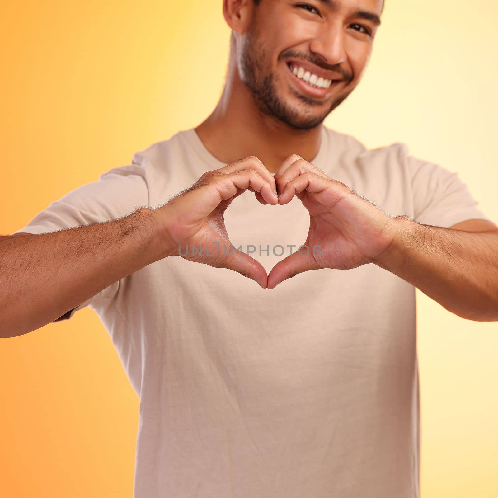 Portrait, heart and hands of man in studio isolated on a yellow background. Love, romance and happy male model with hand gesture for romantic emoji, care symbol or kindness, support or thank you. by YuriArcurs