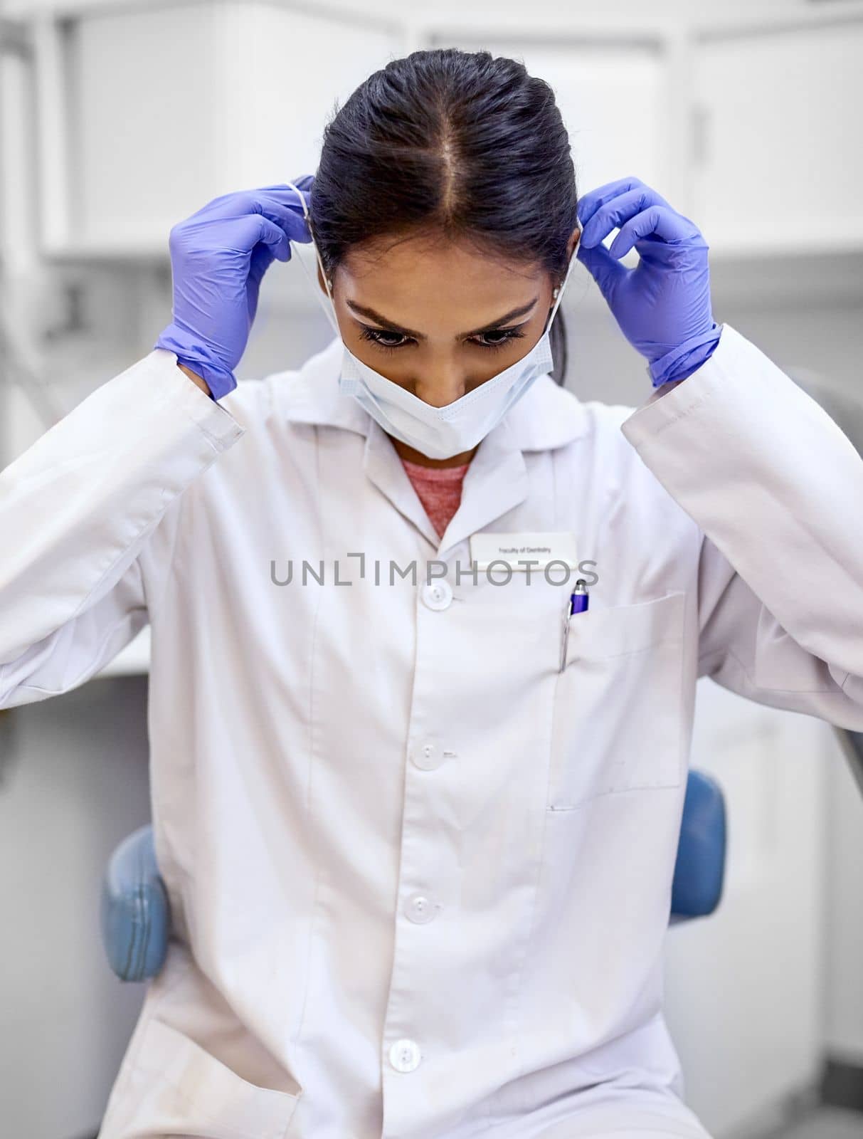Preparing for a surgical procedure. a young female dentist putting on a surgical mask