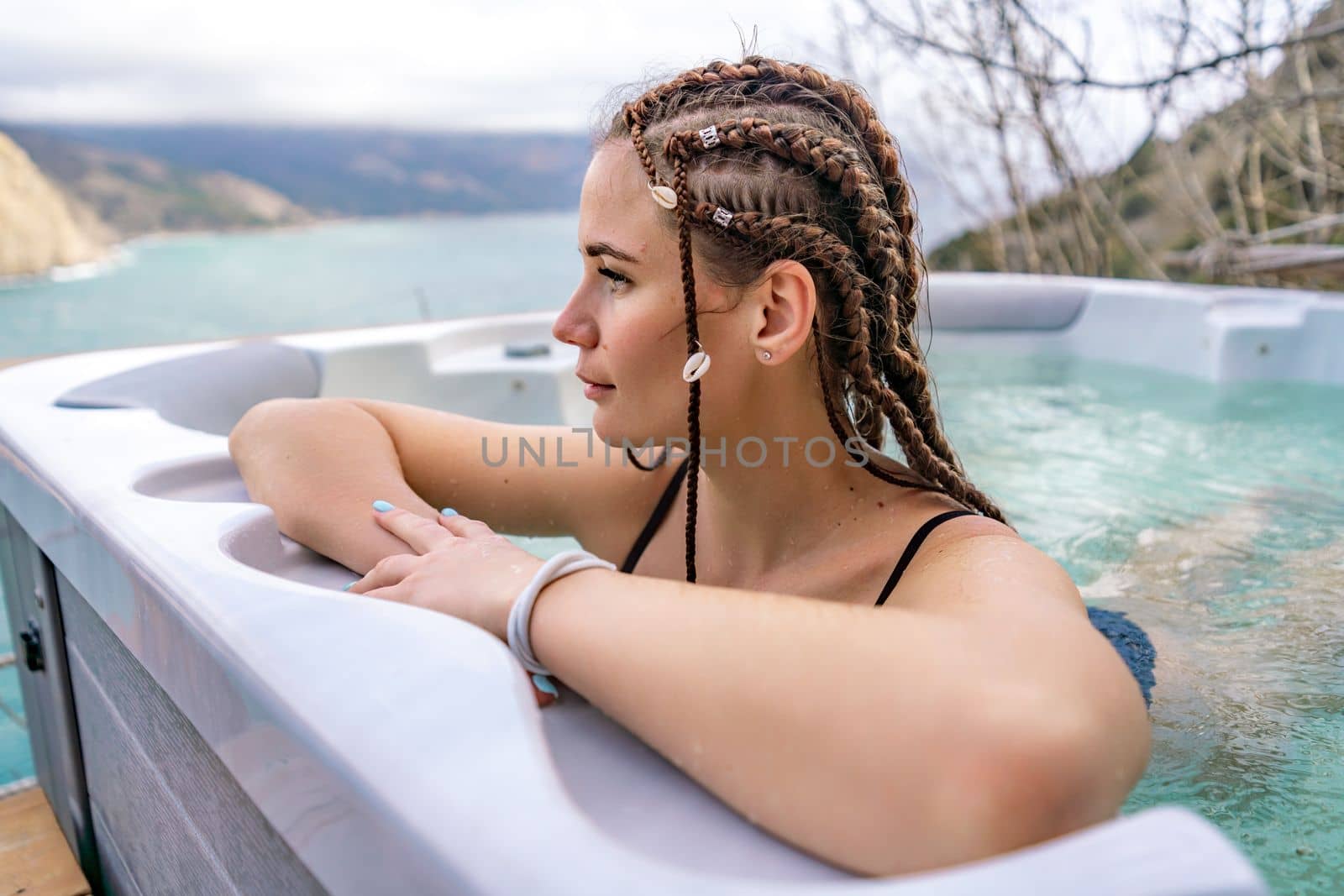 Take time for yourself. Outdoor swimsuit with mountain and sea views. A woman in a black swimsuit is relaxing in the hotel pool, admiring the view.