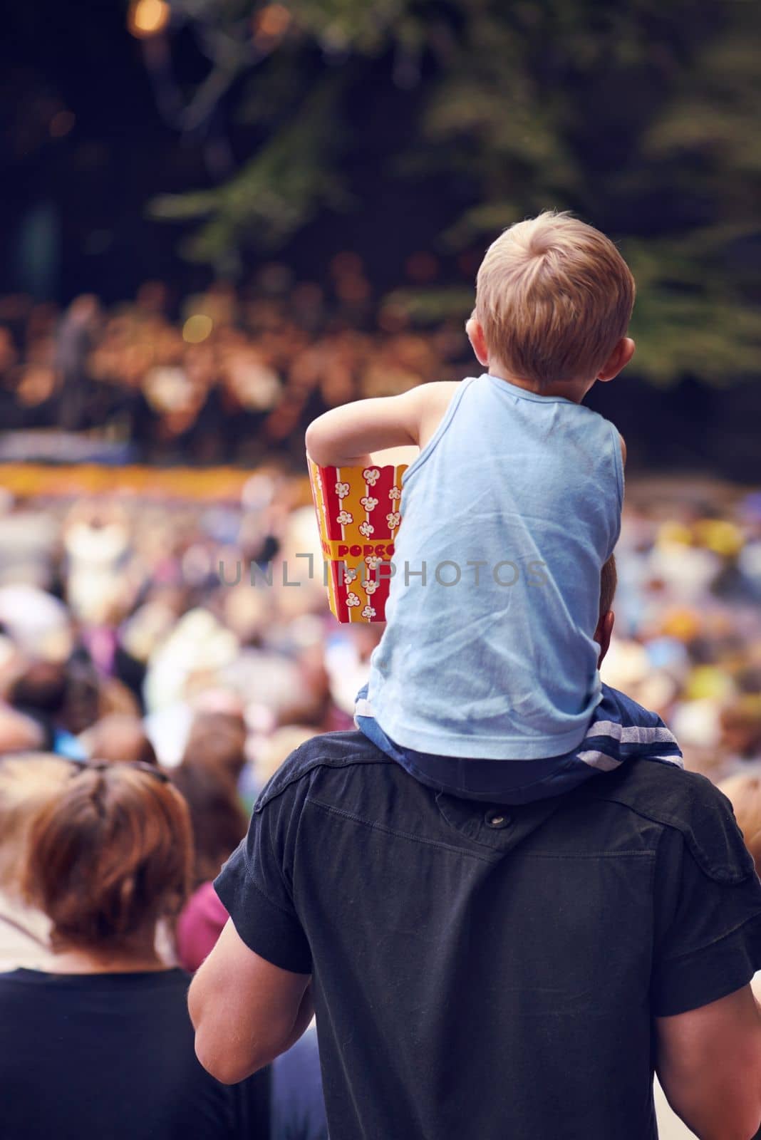Beats and eats. Rearview shot of a young boy sitting on his fathers shoulders at an outdoor festival. by YuriArcurs