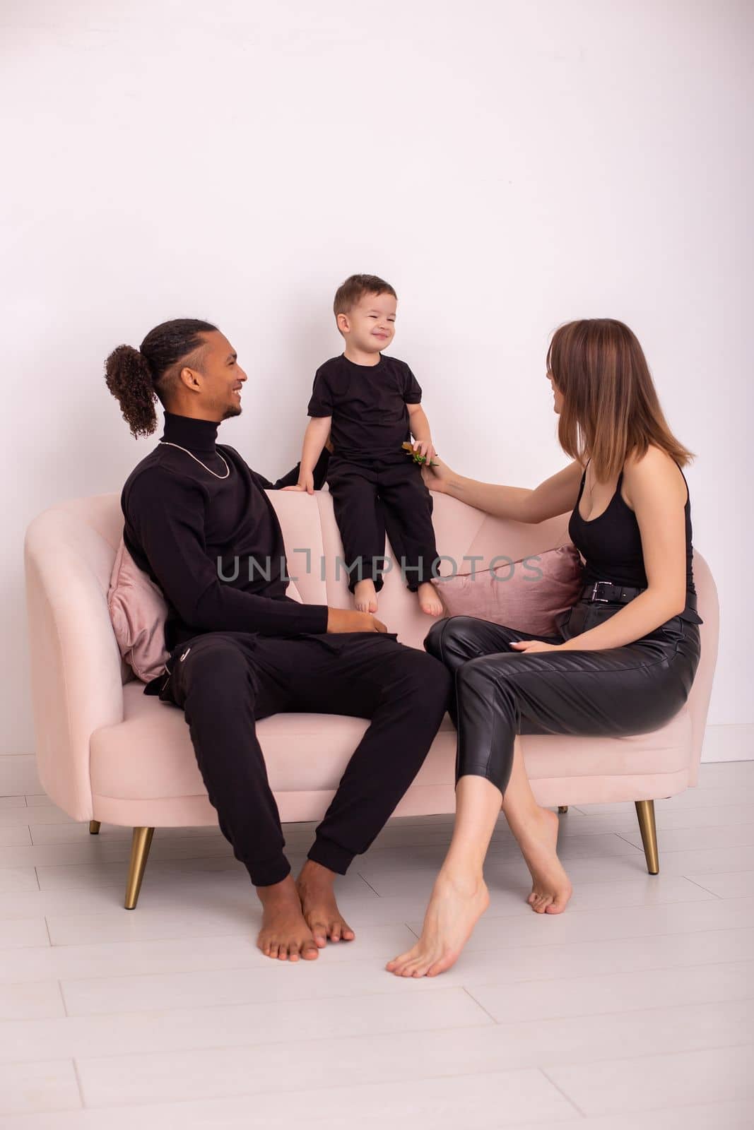 happy family in black clothes, sitting on pink sofa in the light living room by Zakharova