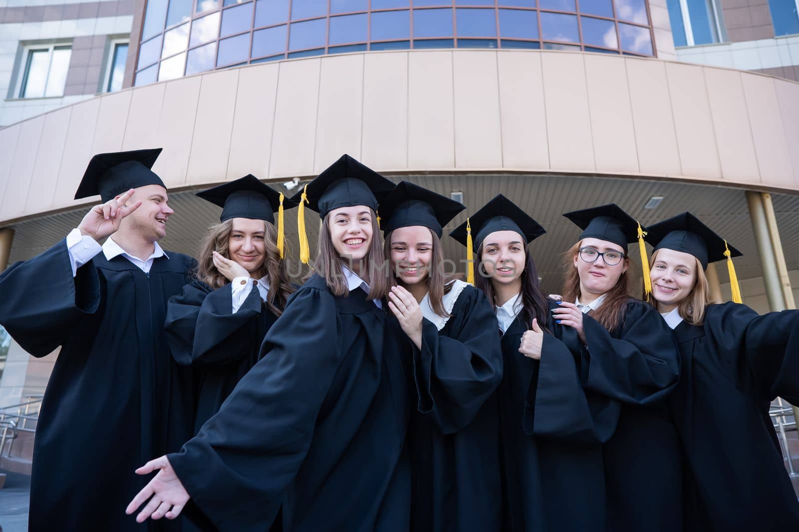 Happy students in graduate gown stand in a row against the backdrop of the university. by mrwed54