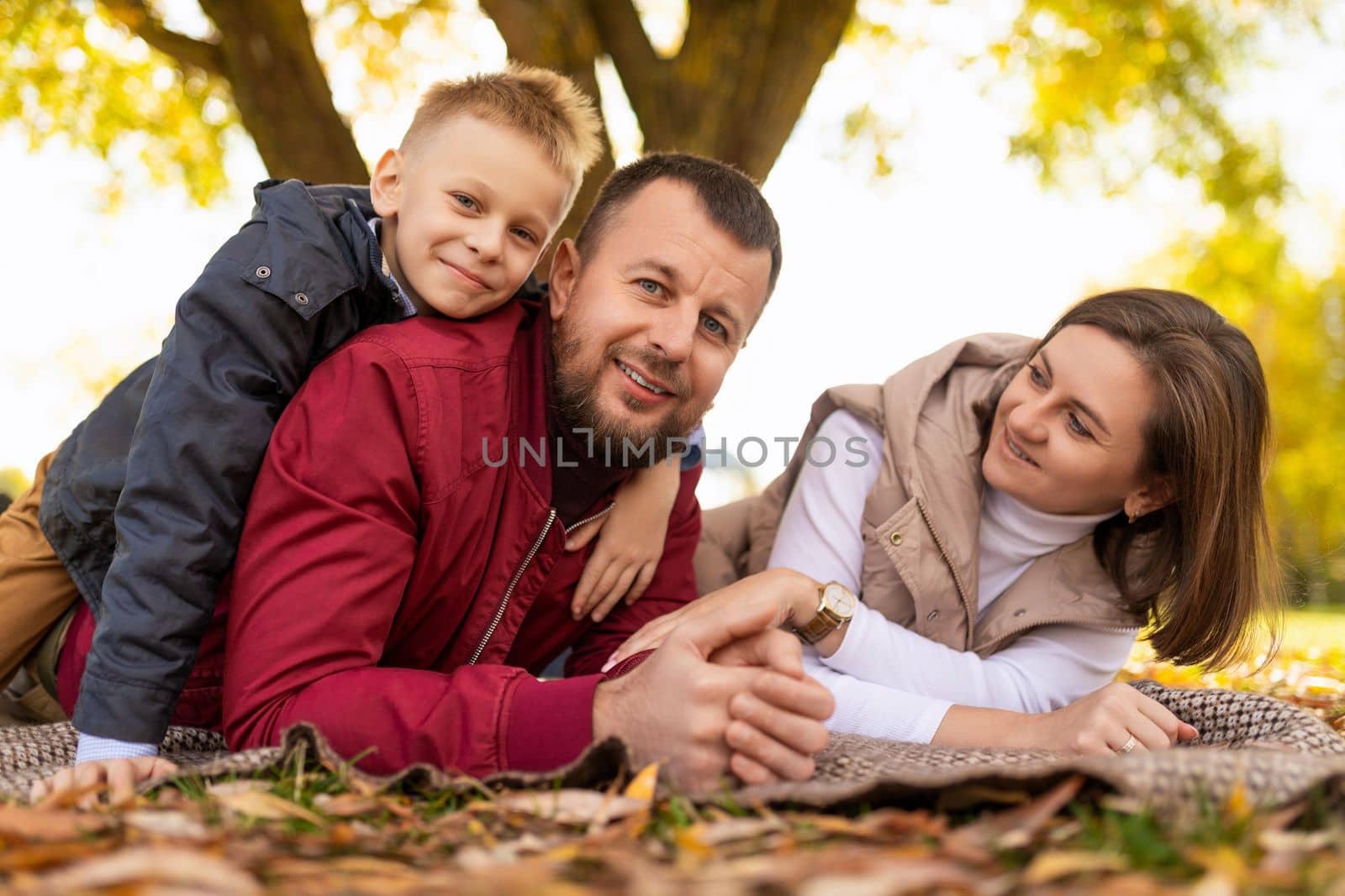 cheerful traditional family with little son lies on autumn leaves in the park with smiles.