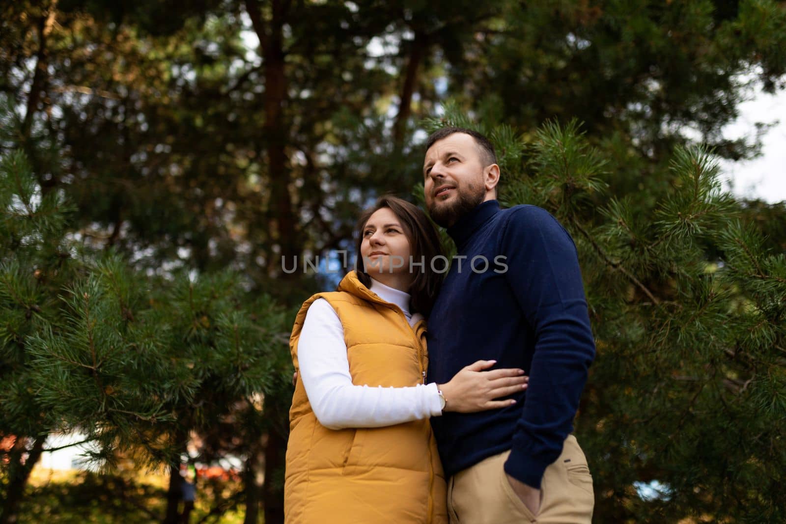 happy adult husband and wife in the autumn forest stand embracing and look into the distance.