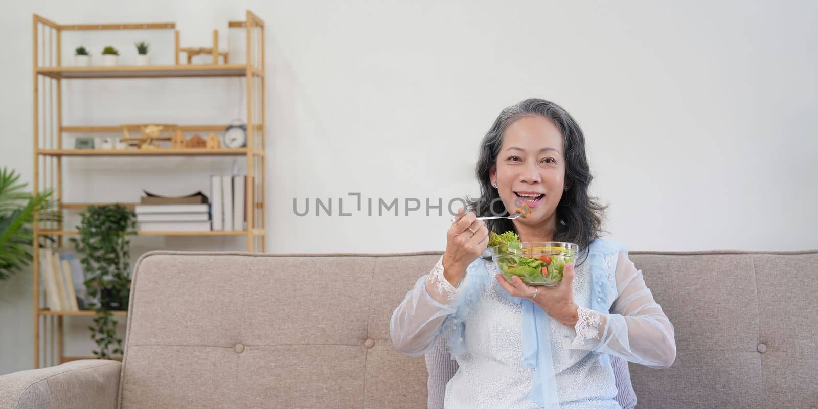 Happy old woman eating healthy vegetable salad at home.