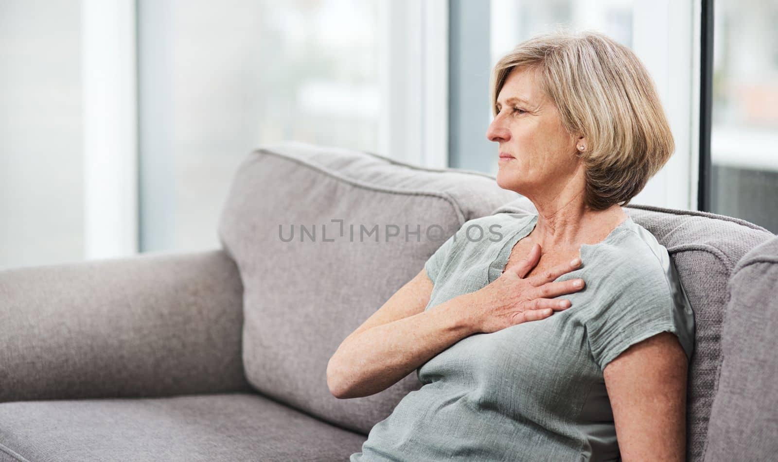 Chest pain is a cause for concern. a senior woman suffering from chest pain while sitting on the sofa at home. by YuriArcurs
