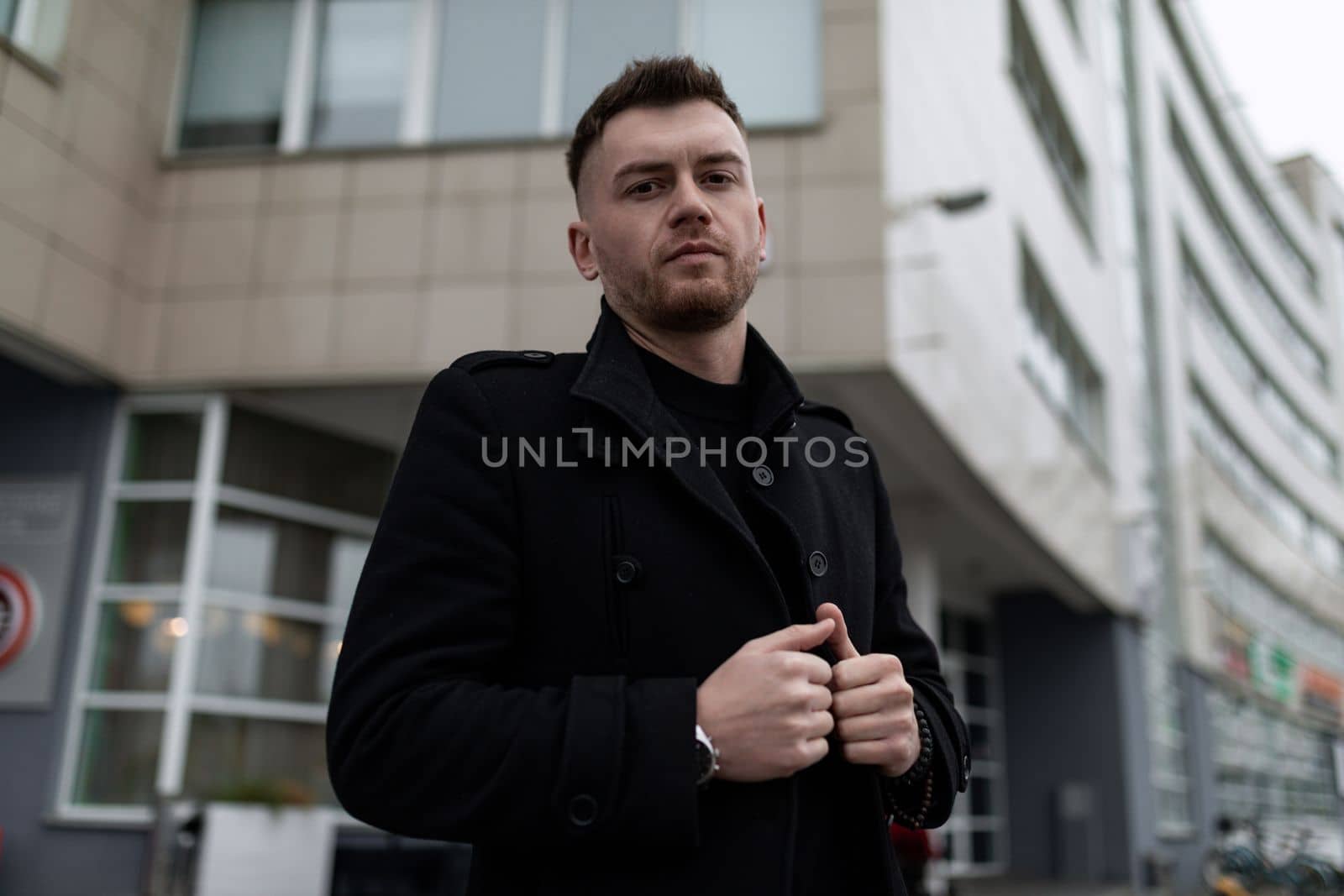 thoughtful brutal man in a stylish coat on the background of the building.