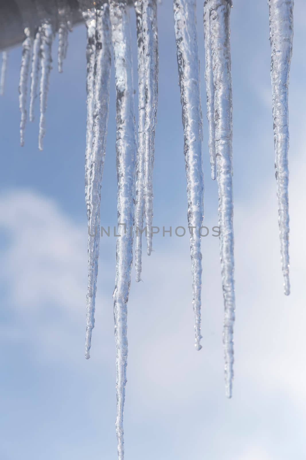 Long icicles of ice hang from the roof of the house. Presented against a background of blue sky with clouds