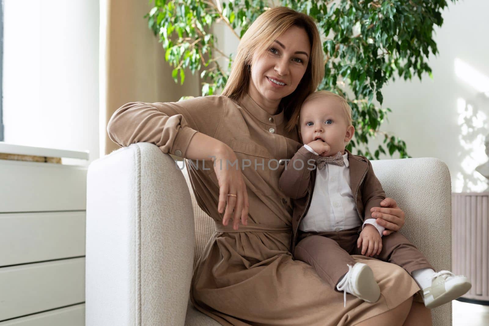 happy mother with her little son are sitting in an armchair in a bright room.