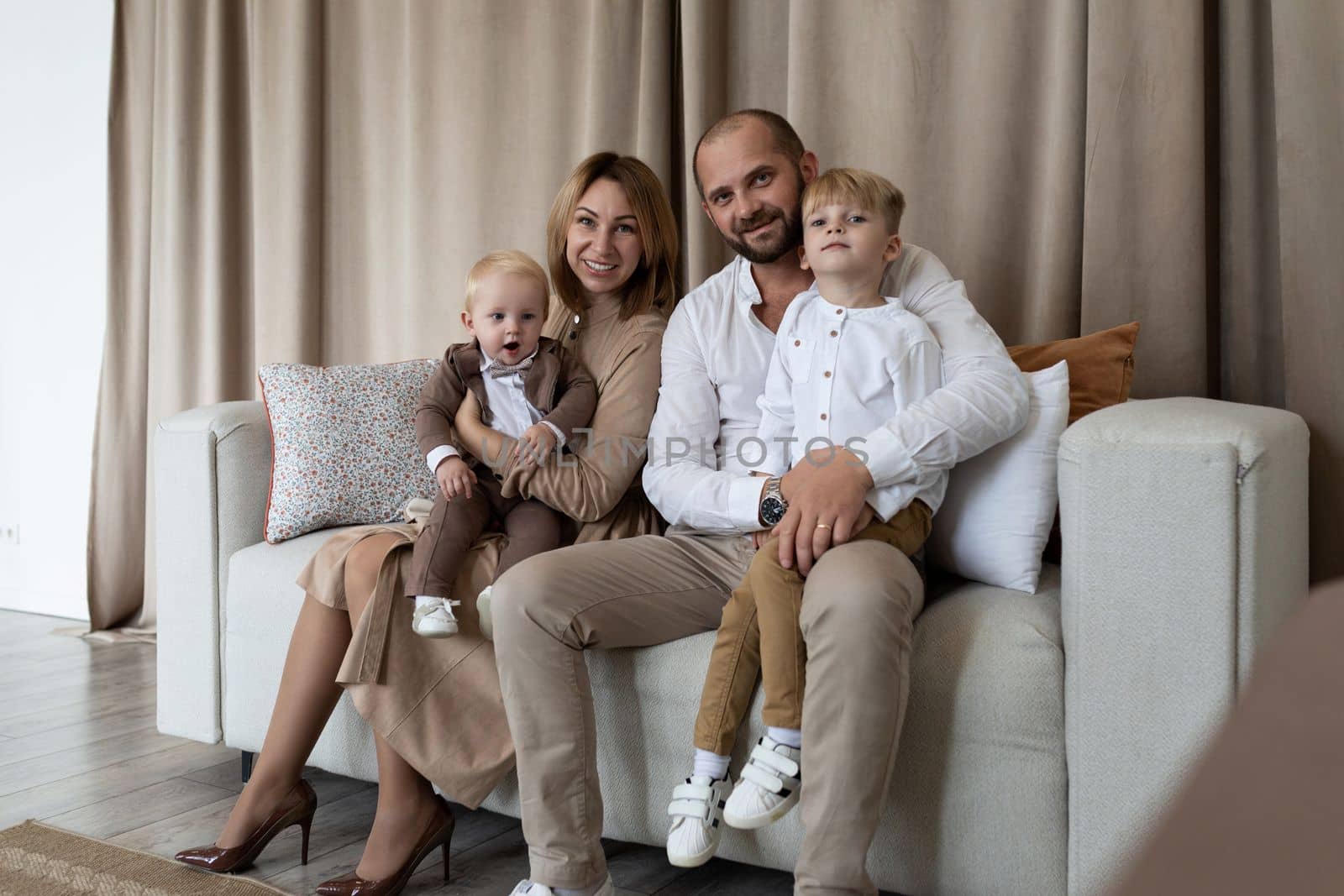 dad mom and two little sons are sitting on the sofa and looking at the camera, Concept of a happy family by TRMK