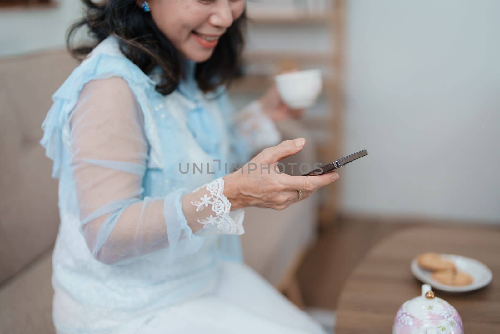 Portrait of an elderly Asian woman holding a mobile phone with eating snacks and drinking tea