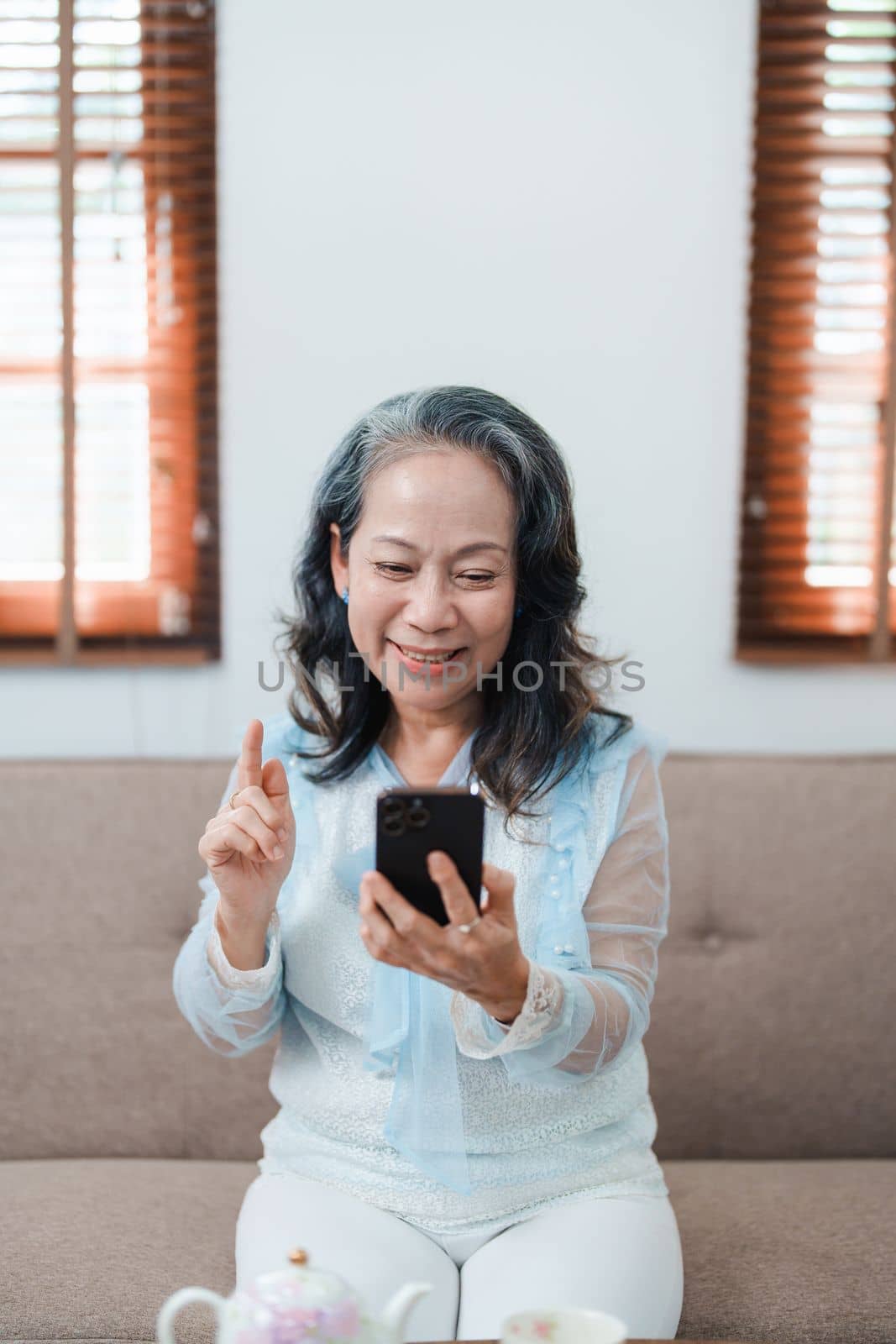 Portrait of an elderly Asian woman holding a mobile phone with eating snacks and drinking tea. by Manastrong
