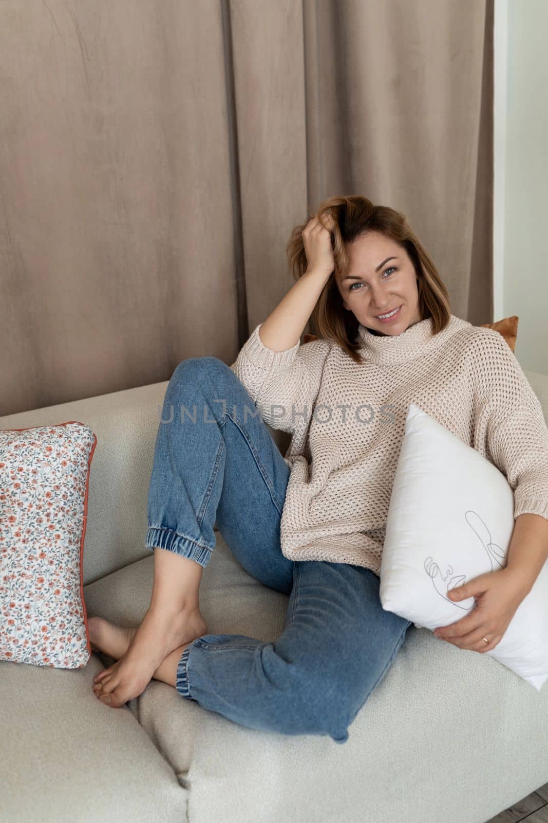 charismatic girl sits on the couch in a comfortable position bend her legs under her.