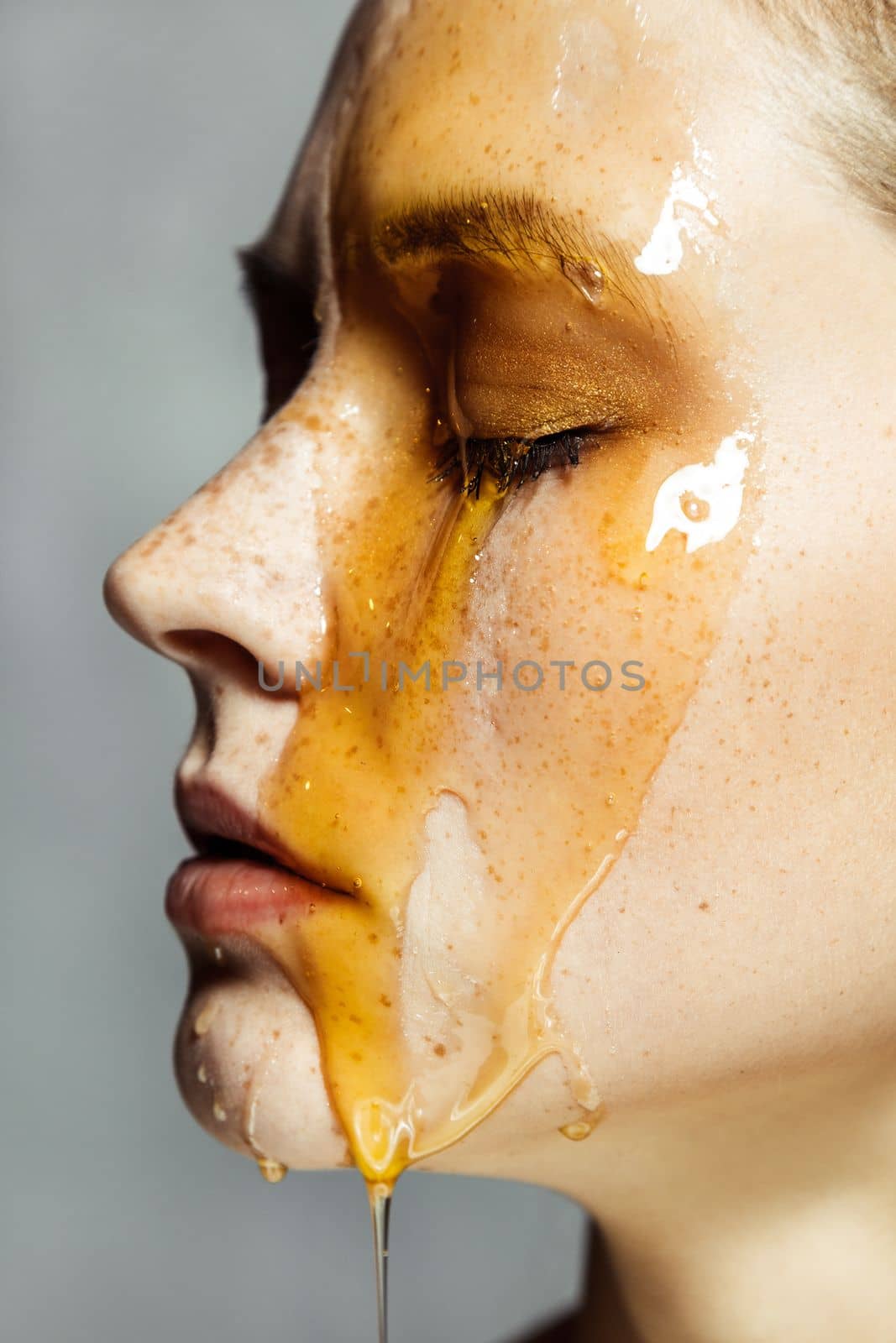 Beautiful serious young brunette woman with freckles, applying honey on face for beauty treatment. by Khosro1