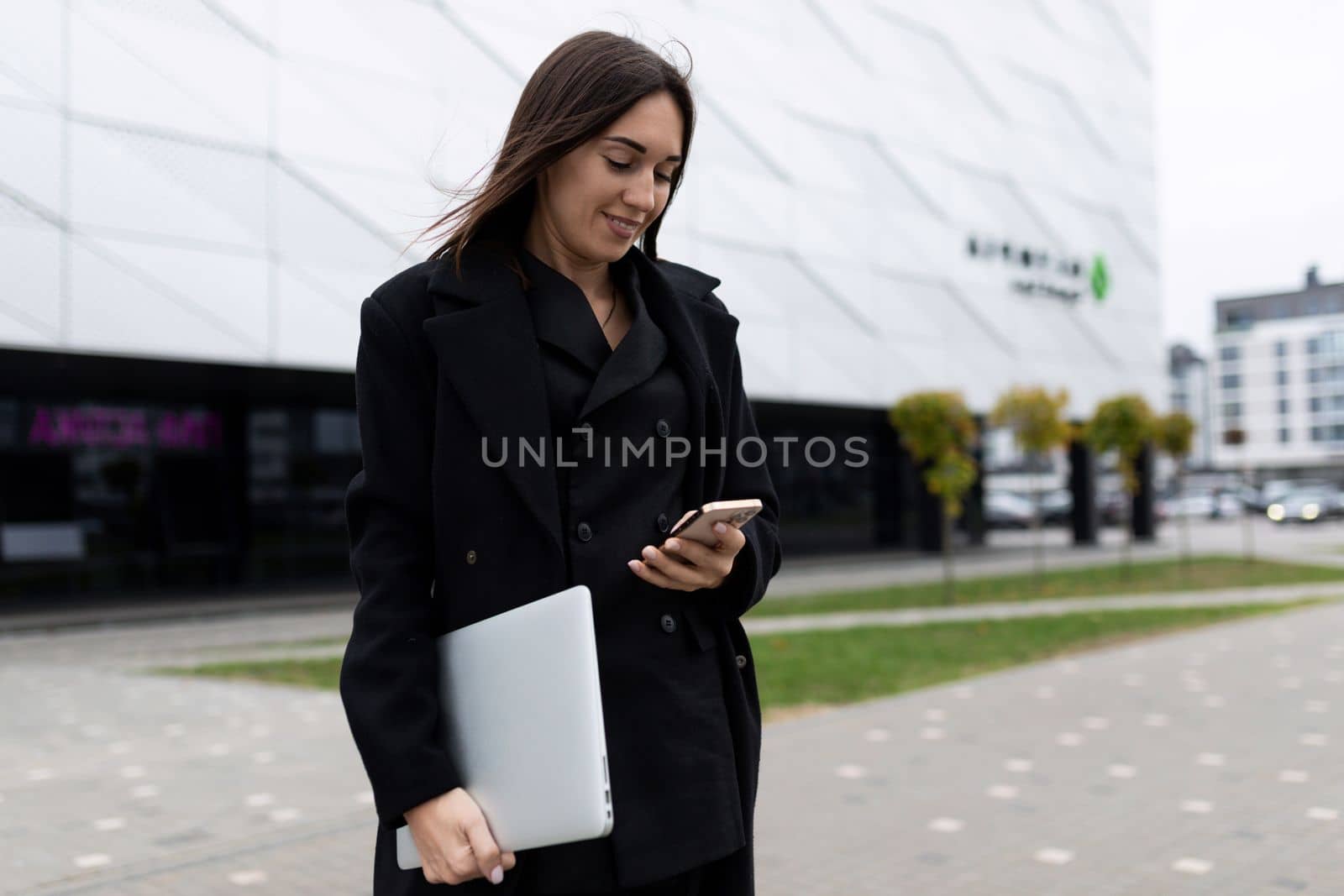 woman Businessman with a laptop in his hands looks at a mobile phone on the background of an office building.