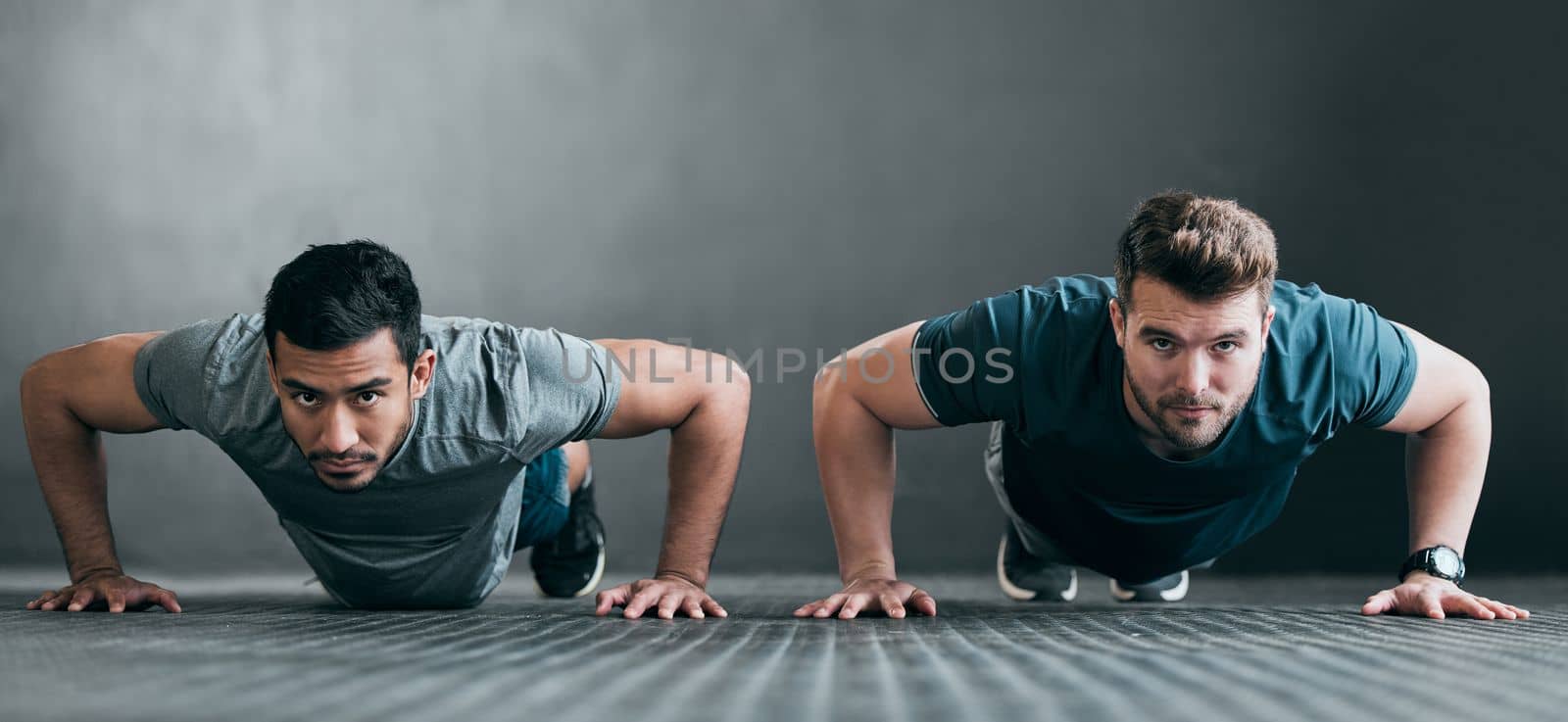 Working on their upper body. Full length portrait of two handsome young male athletes doing pushups side by side against a grey background