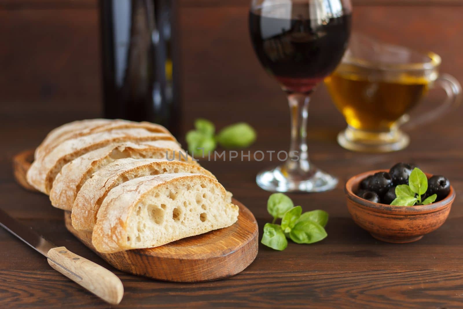 Sliced ciabatta with red wine, olive oil, olives and basil on a wooden background. by lara29