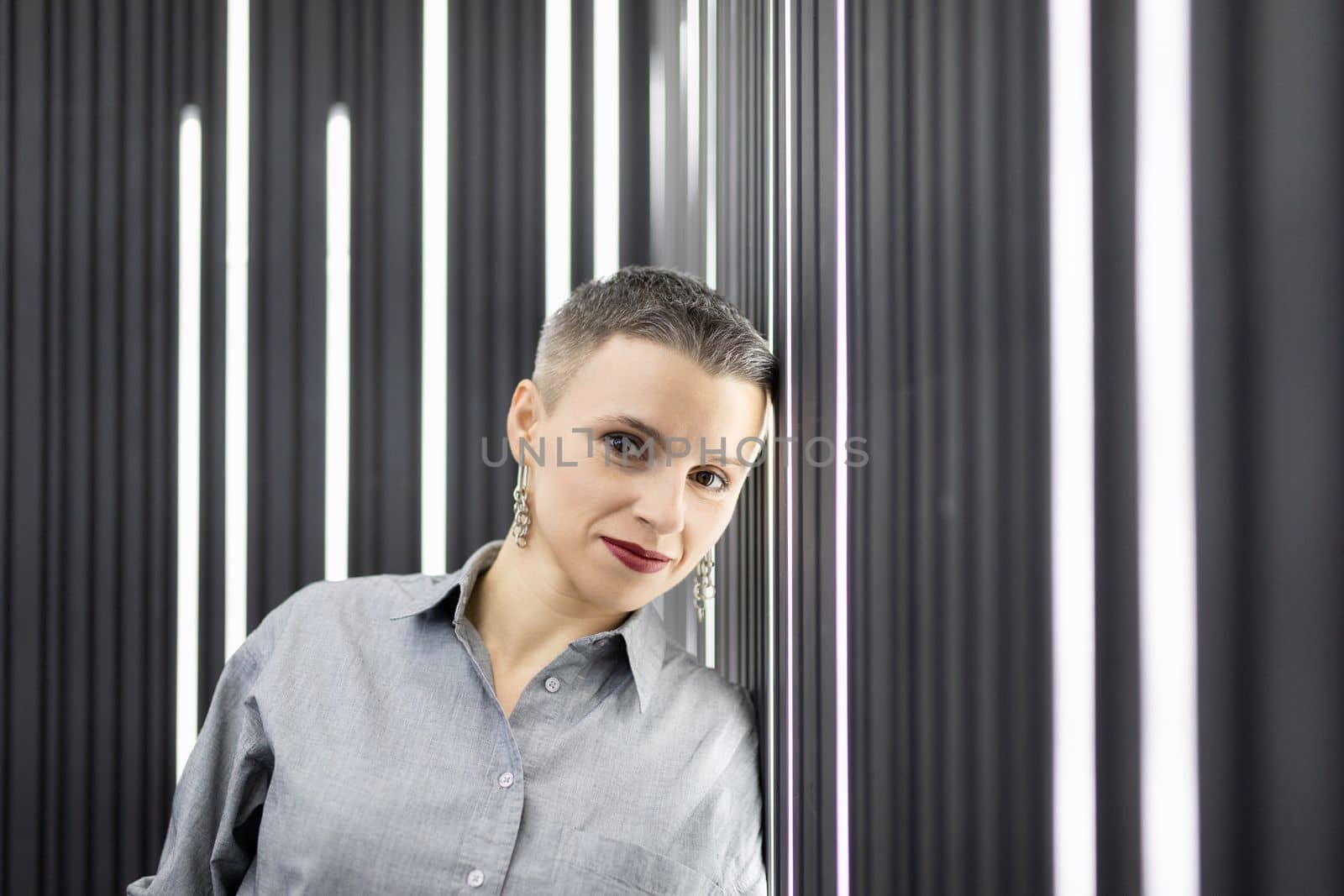 portrait of a strong caucasian adult woman against the background of a wall with vertical lamps.