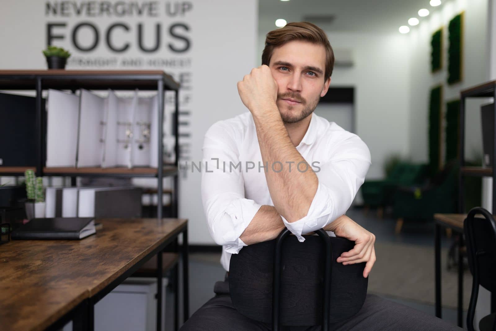 Caucasian manager sits on a chair and looks forward tired.