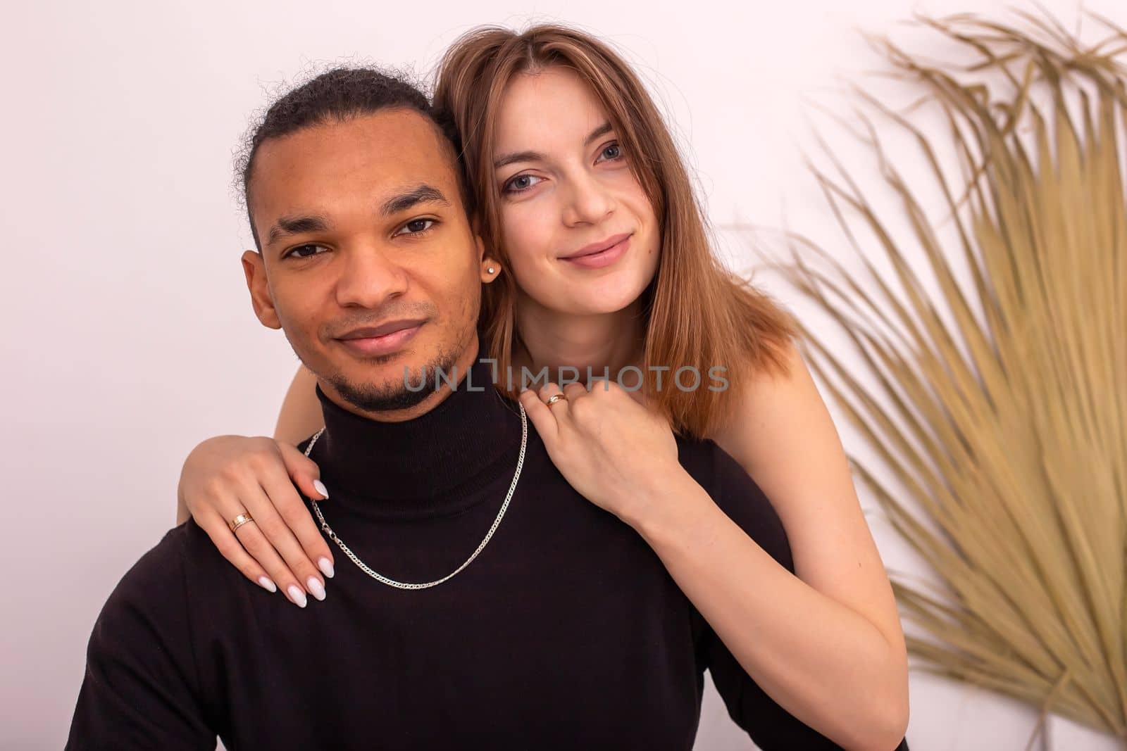 Portrait of beautiful , multiracial couple, in black clothes, are sitting near the wall in the room. by Zakharova