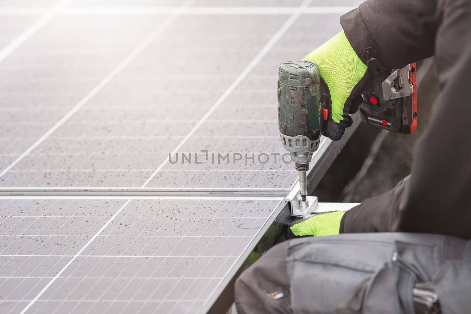 The solar panel installer twists the modules together using aluminum fasteners and a cordless drill. Rooftop installation work and security, concept with copy space by SERSOL