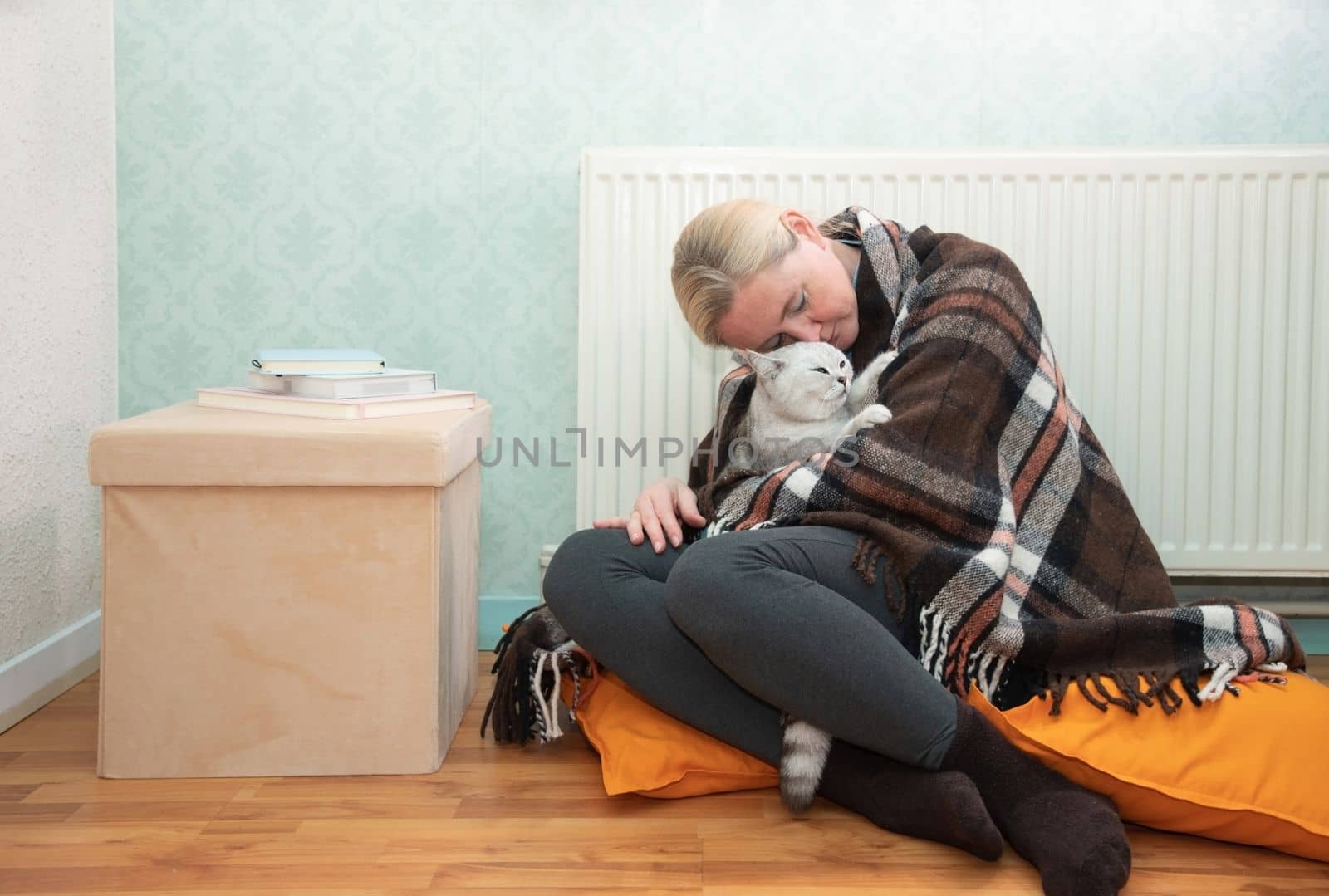 Woman sitting with cat under blanket warming near an electric heater, Cat makes blonde lady happy sitting near heating radiator High quality photo