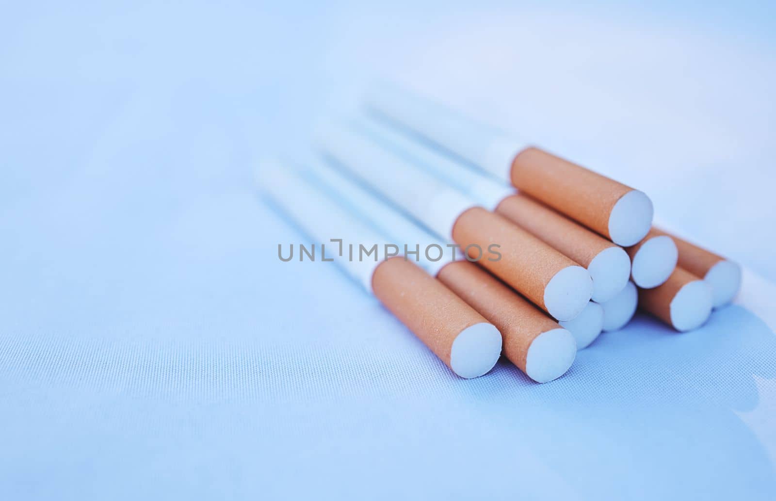 Cigarette, cancer and smoke with a tobacco product on the ground against a blue background to promote awareness. Smoking, toxic and addiction with cigarettes in a pile or stack on the floor.