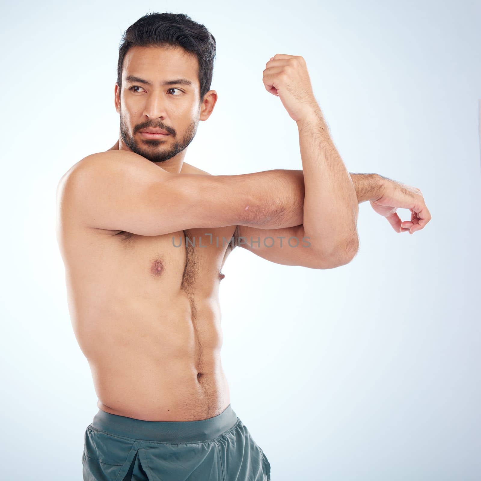 Health, fitness and man stretching arm for flexibility in studio isolated on a blue background. Thinking, sports and young male athlete, warm up and getting ready for training, exercise and workout