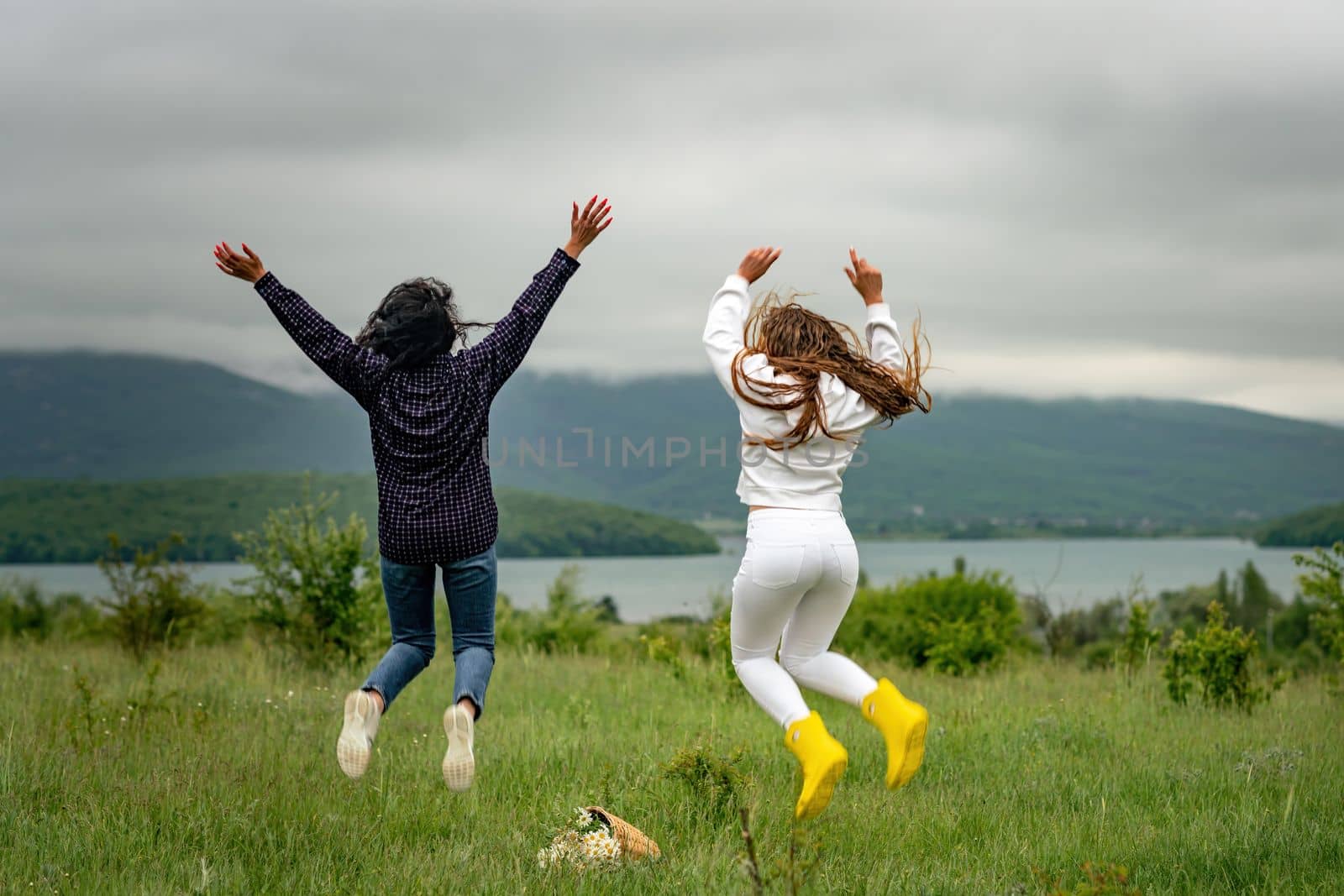 Two girls with long hair are jumping in a clearing overlooking the mountains. The concept of travel and tourism to different countries. by Matiunina
