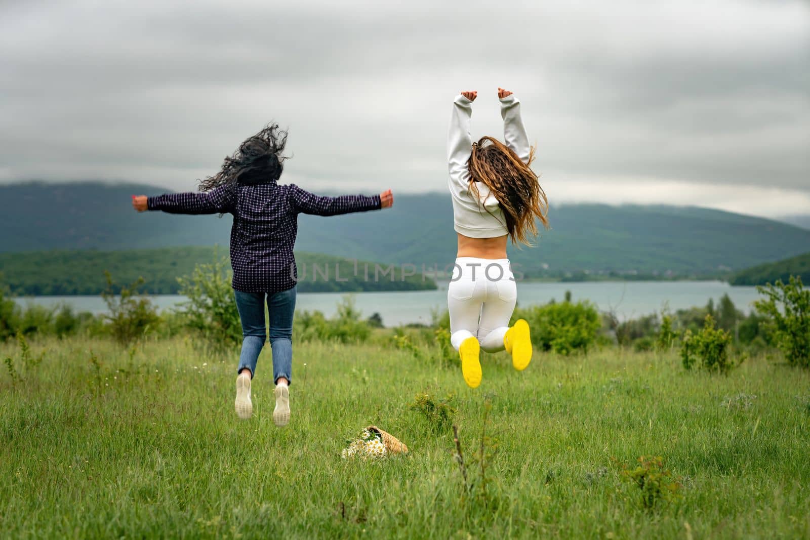 Two girls with long hair are jumping in a clearing overlooking the mountains. The concept of travel and tourism to different countries
