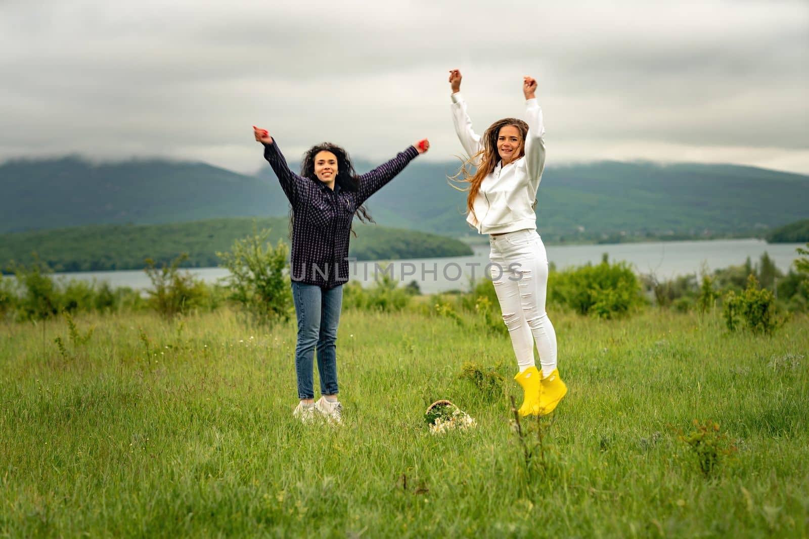 Two girls with long hair are jumping in a clearing overlooking the mountains. The concept of travel and tourism to different countries