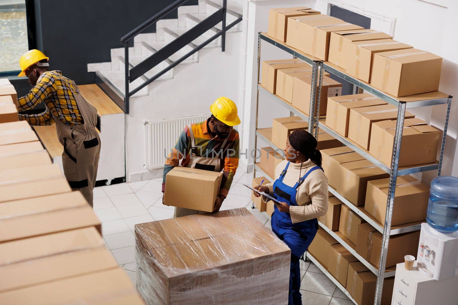 Package handler holding parcel and talking with supervisor in warehouse. African american logistics manager inspecting freight transportation and checking cardboard box in storehouse