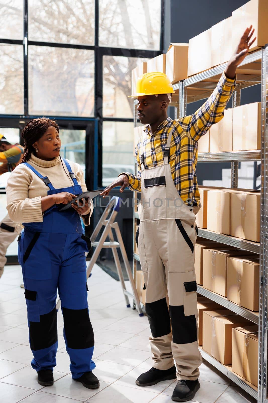 African american warehouse worker explaining supervisor packages storage system, showing on parcels shelf and talking. Storehouse manager listening to colleague and holding digital tablet
