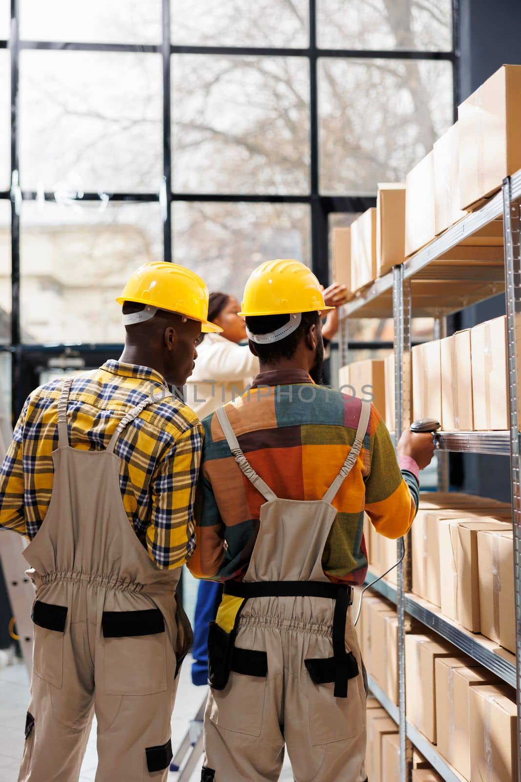 African american storehouse employees analyzing goods in stock using barcode scanner. Merchandise managers wearing protective helmets scanning cardboard boxes with retail products in warehouse