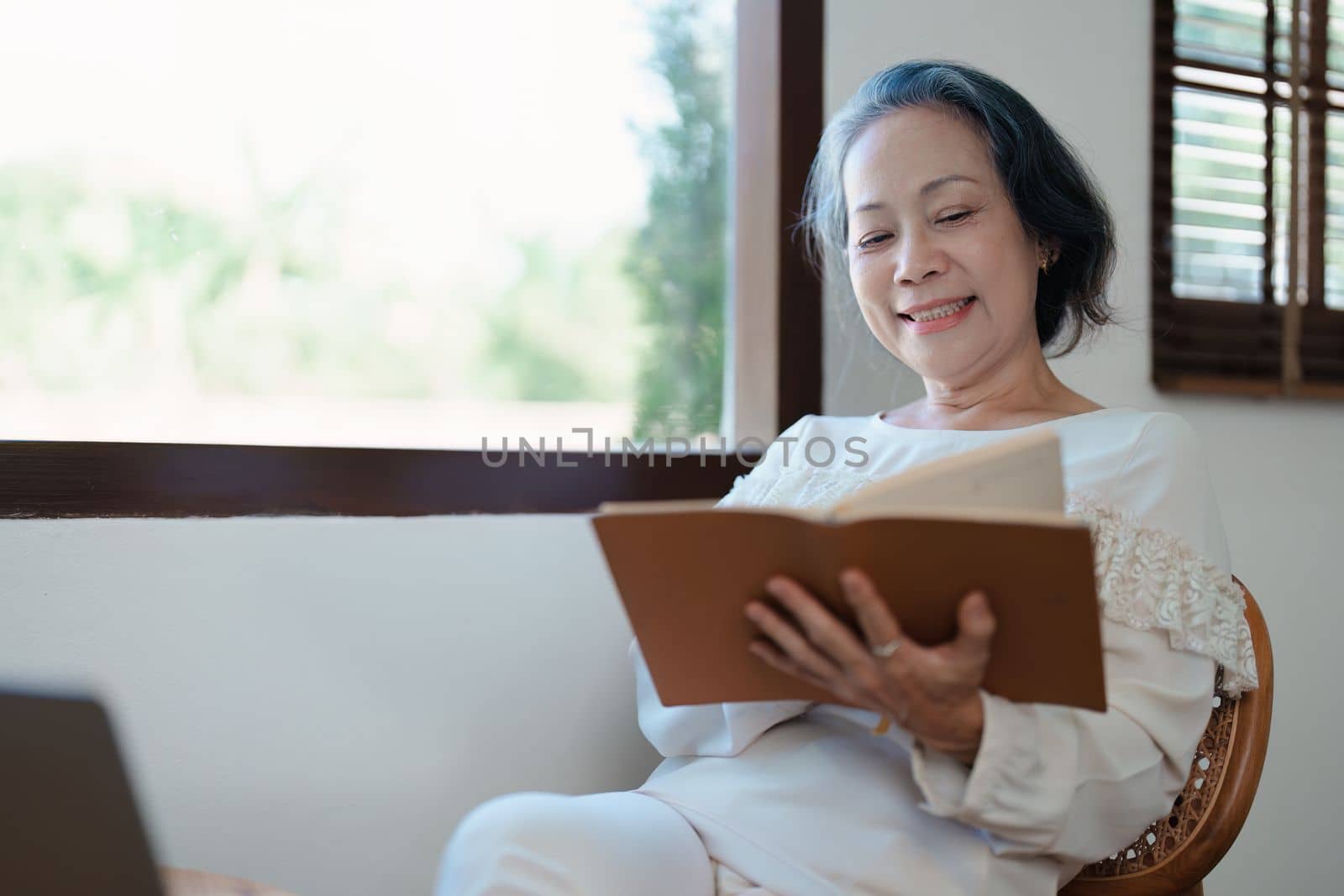 Portrait of an elderly Asian woman in a modern pose holding a memory notebook and operating a computer