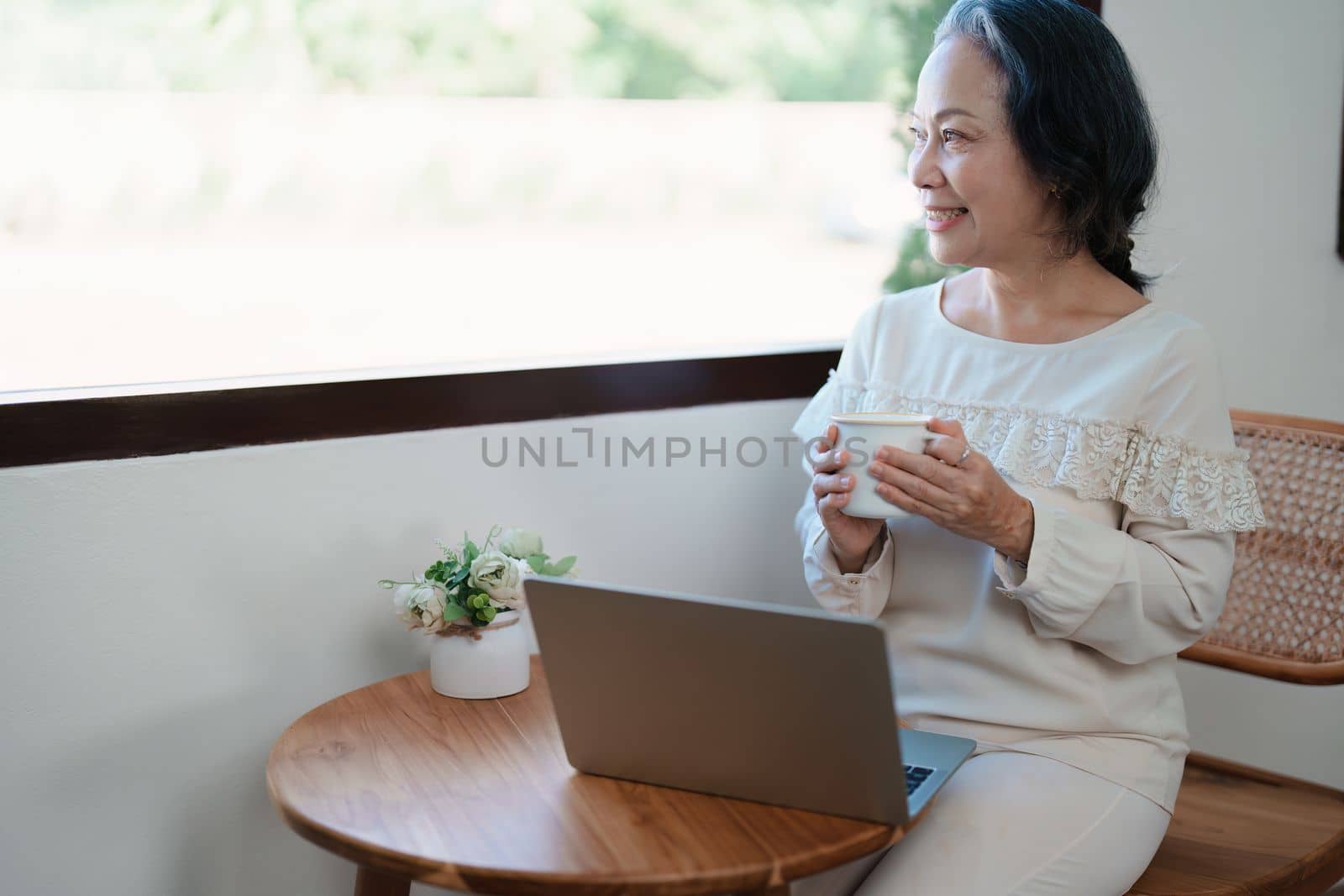 Portrait of an elderly Asian woman in modern pose doing computer work and drinking coffee
