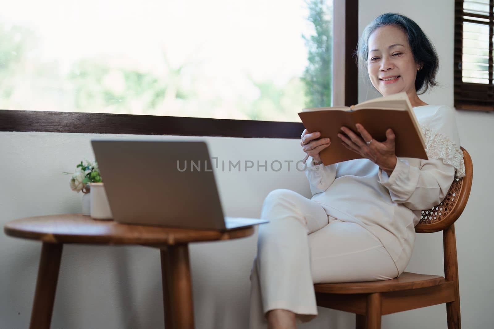 Portrait of an elderly Asian woman in a modern pose holding a memory notebook and operating a computer