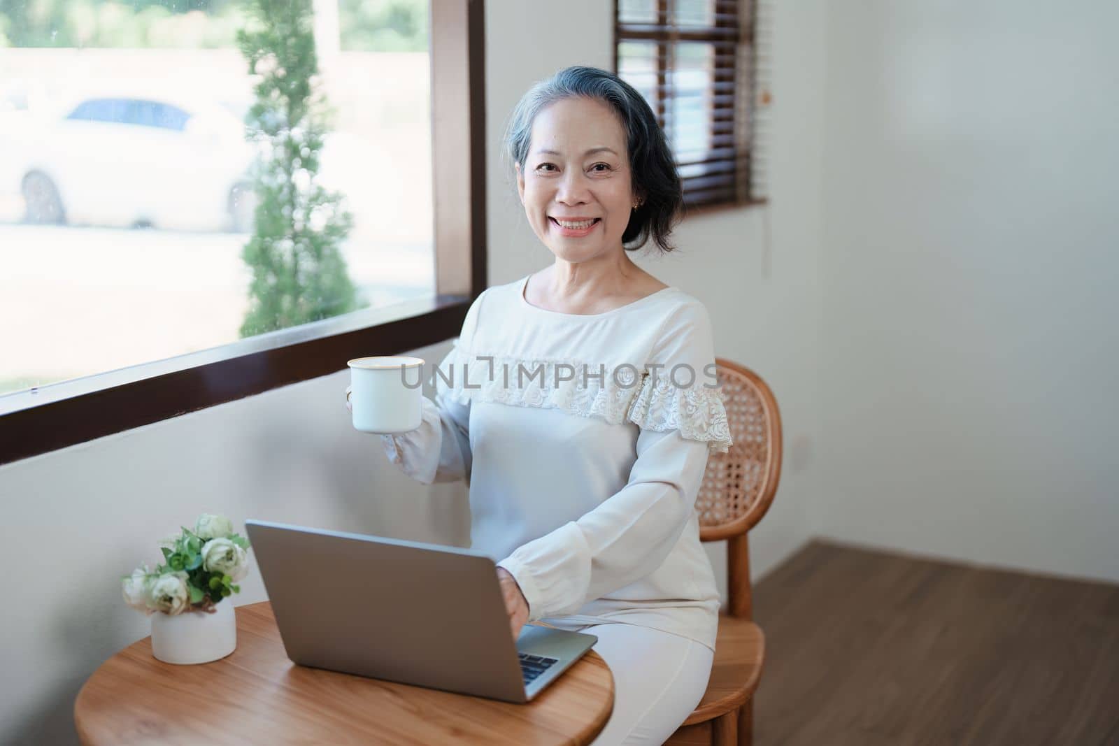 Portrait of an elderly Asian woman in modern pose doing computer work and drinking coffee