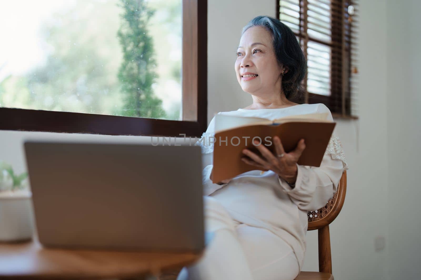 Portrait of an elderly Asian woman in a modern pose holding a memory notebook and operating a computer